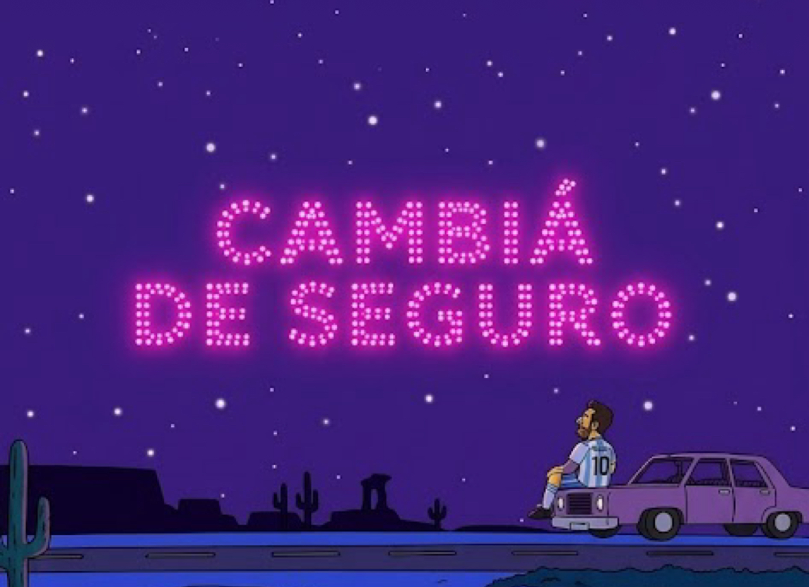 Cartel de neón rosa que dice CAMBIÁ DE SEGURO sobre un auto en el desierto, a la noche